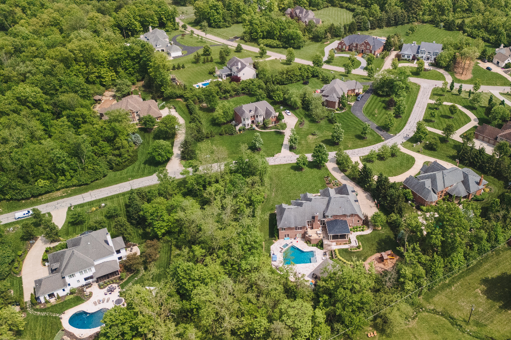 Indian Hill Ohio - ABS Services Aerial view of a suburban neighborhood with winding roads, green lawns, and several houses with swimming pools in backyards.