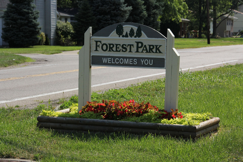 Forest Park entrance sign in a grassy median with a flower bed, saying 'Forest Park welcomes you' by a street.